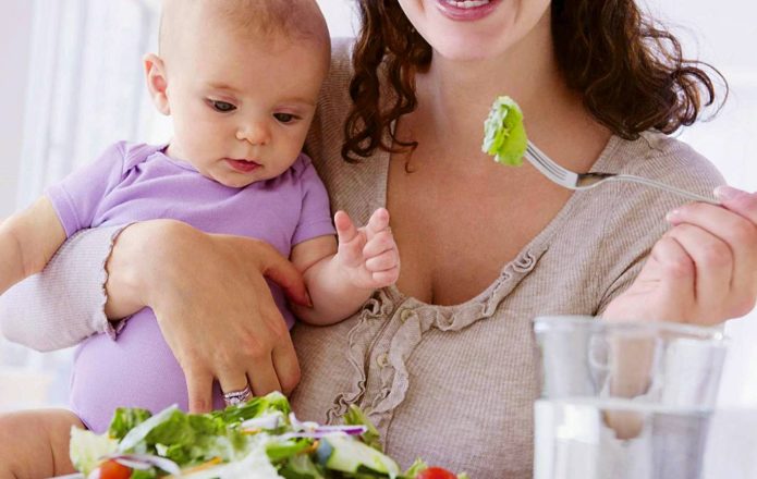Женщина держит на руке ребёнка и ест салат