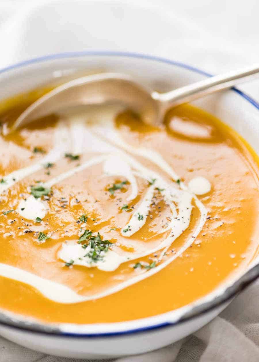 Thick and creamy pumpkin soup in a rustic white enamel bowl with a silver spoon, ready to be eaten.