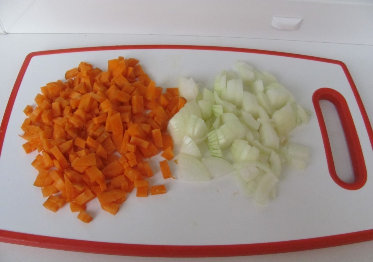 нарезанные морковь и репчатый лук на белой разделочной доске на столе